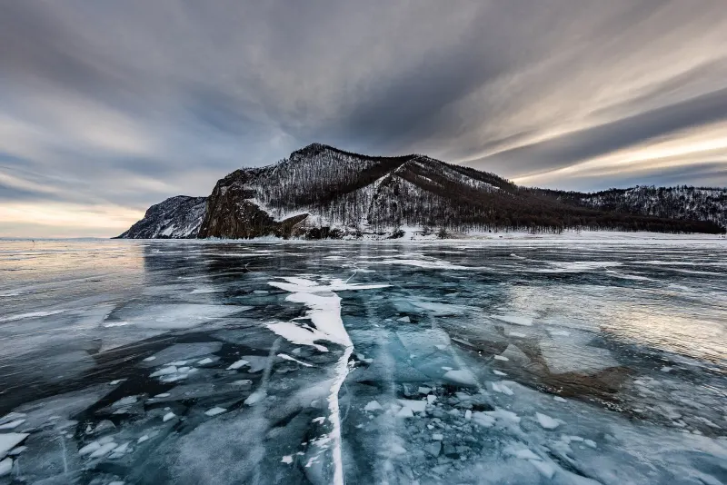 Baikal in winter: clear cracked ice and a rocky headland